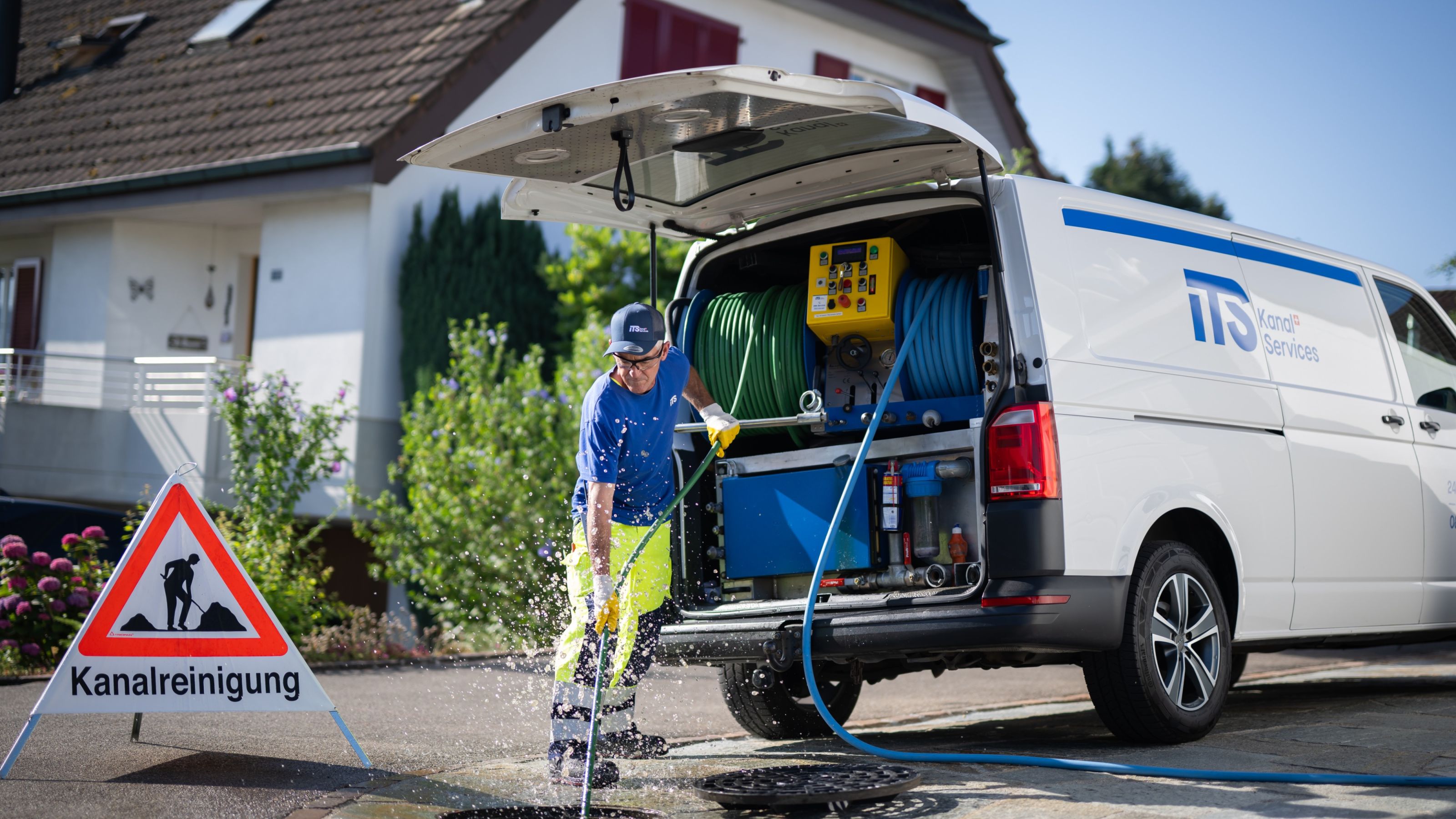 Mitarbeiter der iTS spült eine Leitung an einem Schacht vor einem Einfamilienhaus, daneben der Servicewagen